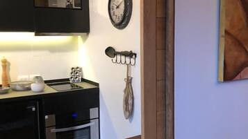 Una cucina con forno a microonde, forno e lavello. C'è una sveglia a muro e un portachiavi appeso al muro.