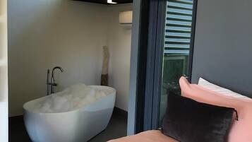 Un dormitorio moderno con una bañera grande, una cama con almohada rosa y negra, y vistas a través de una ventana.