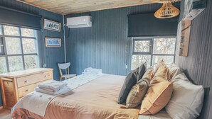 A bedroom with a bed, a desk, and a chair. There are windows and a ceiling fan.