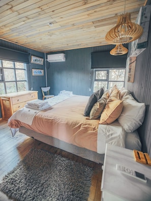A bedroom with a bed, a desk, and a chair. There are windows and a ceiling fan.