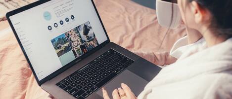 A person using a laptop on a bed with a cup of coffee nearby.