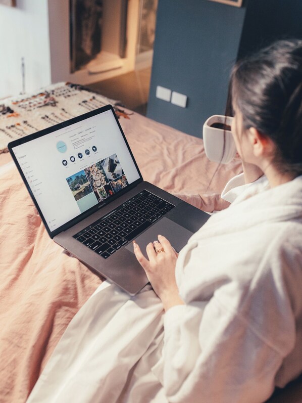 A person using a laptop on a bed with a cup of coffee nearby.