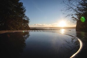 A calm body of water reflecting the sky and trees, with a clear horizon and a bridge in the distance.