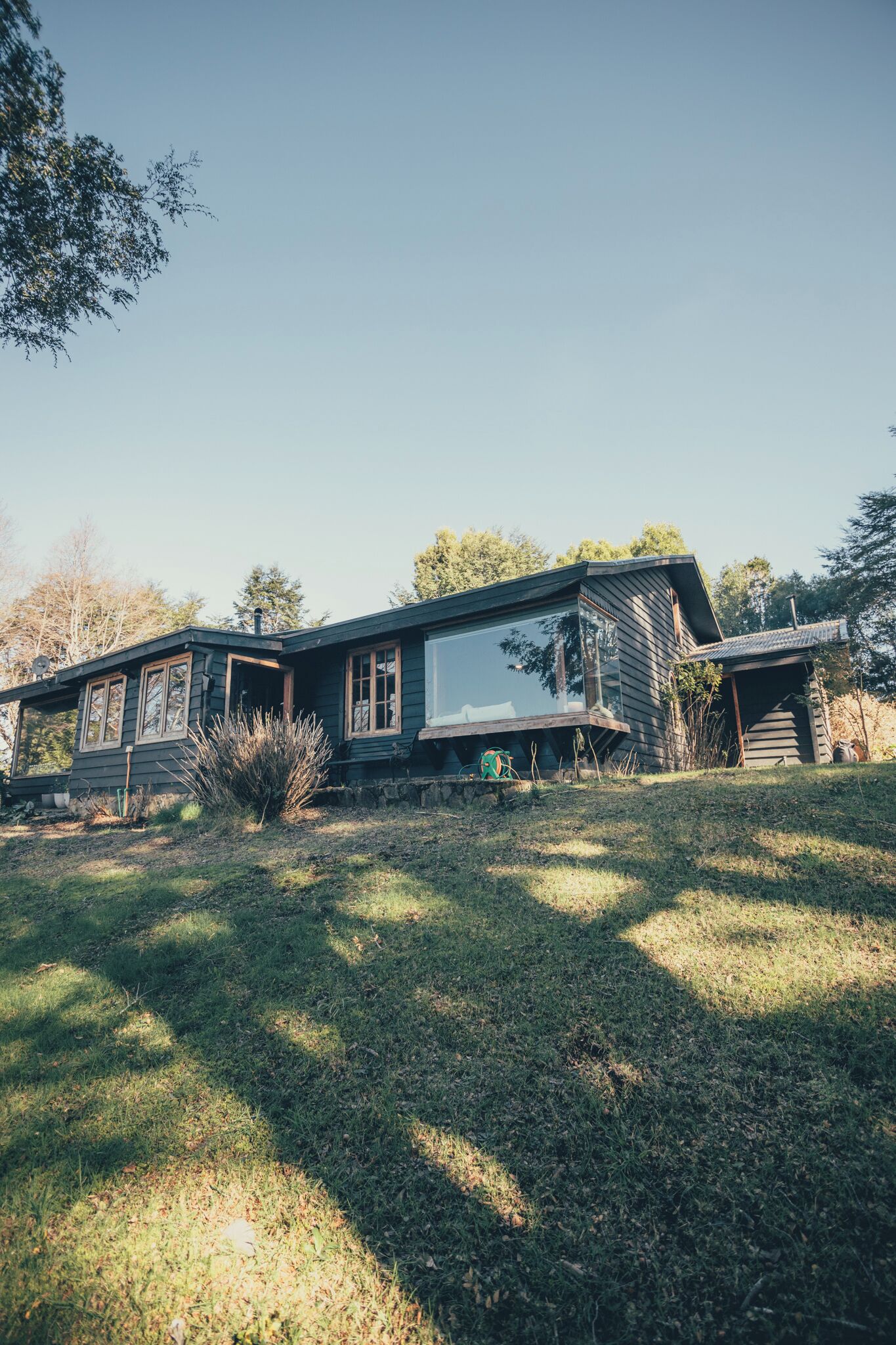 Una casa moderna con un amplio ventanal, un muro de piedra y un patio cubierto de césped.