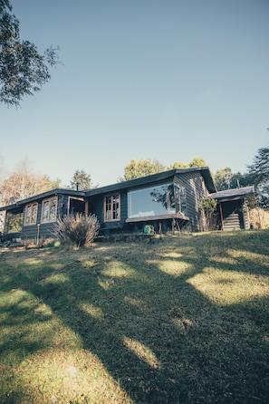 A modern house with a large glass window, a stone wall, and a grassy yard.