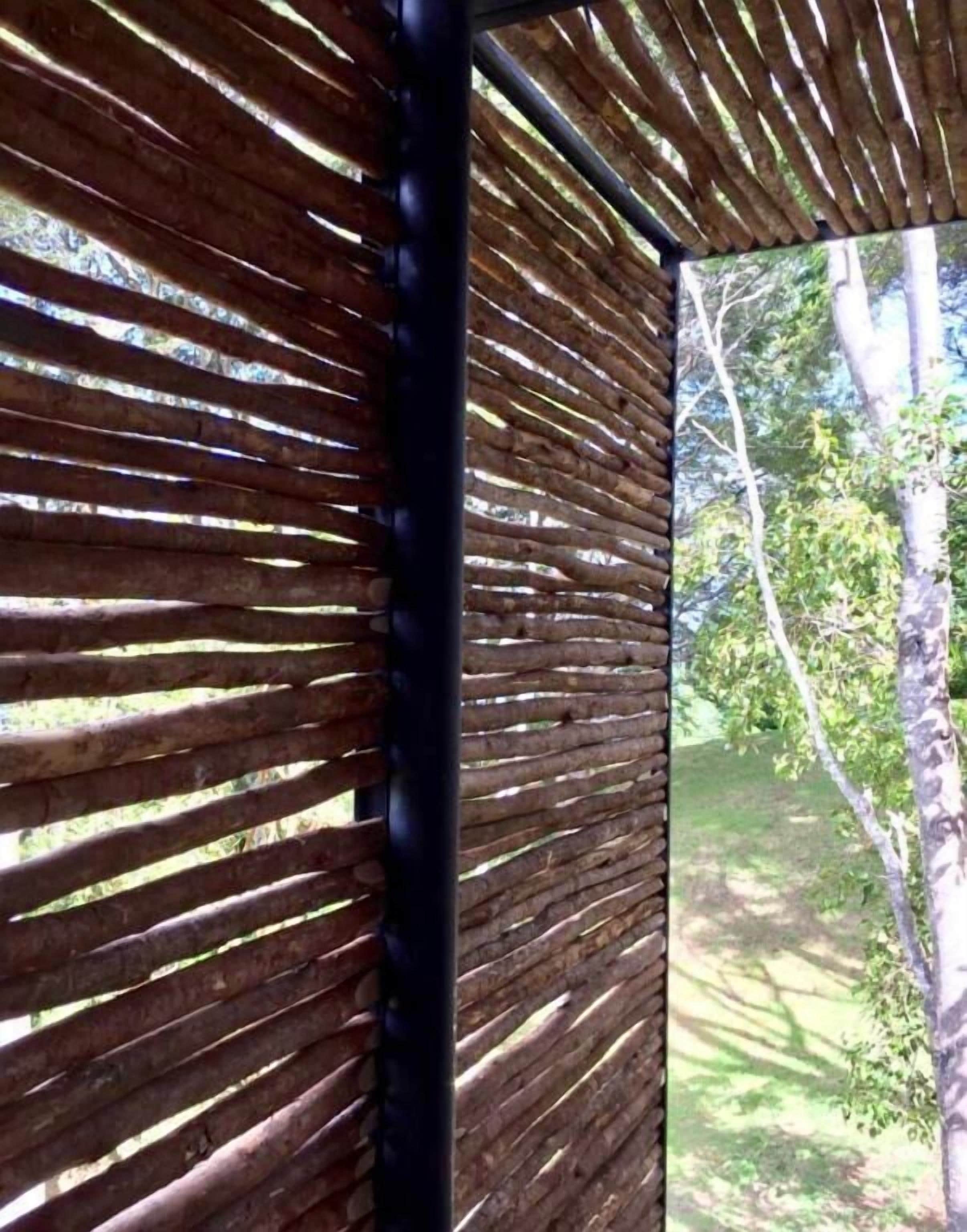 Una estructura de madera con listones que ofrece vistas a un espacio natural al aire libre.