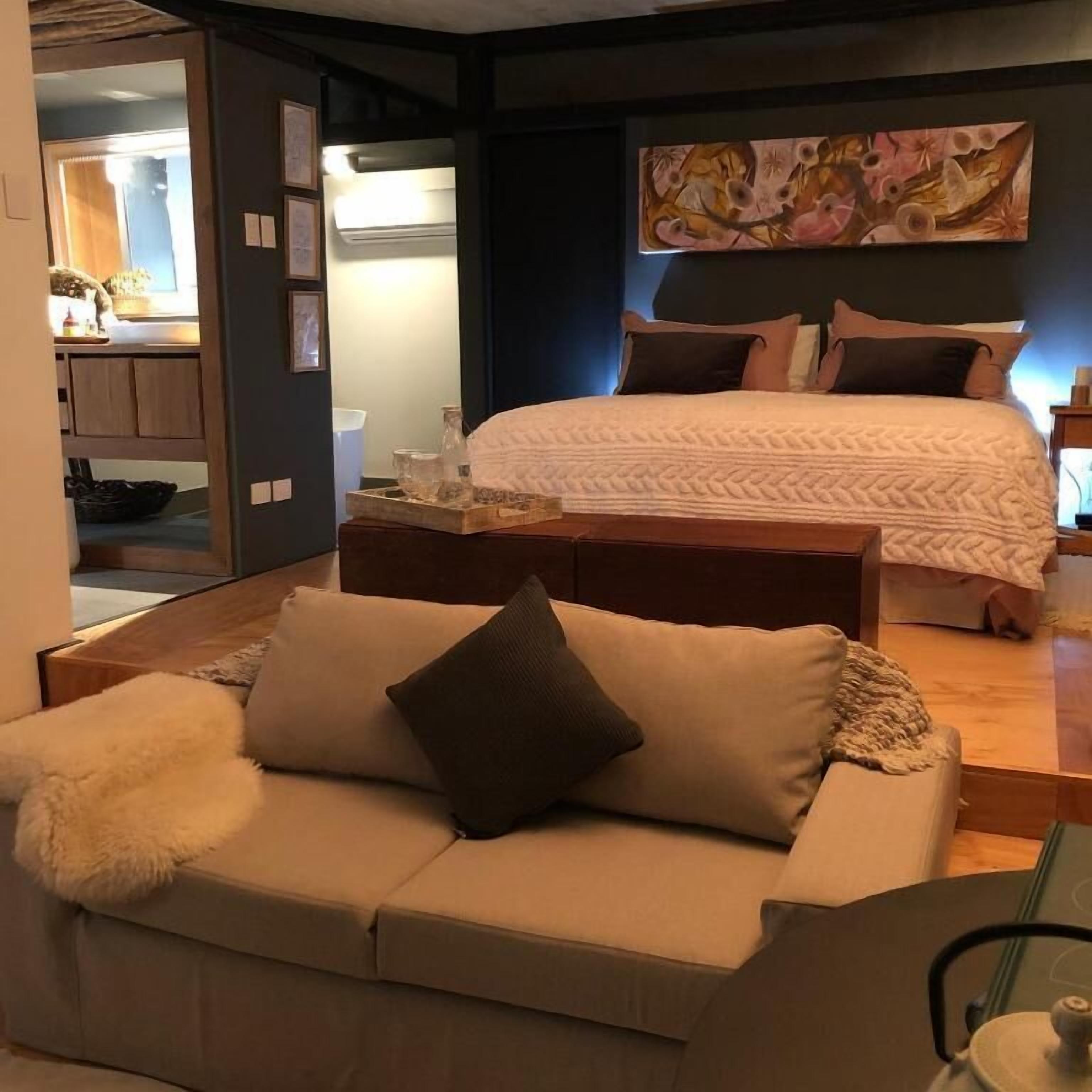 A bedroom with a bed, a bedside table, a nightstand, a sofa, and a painting on the wall.