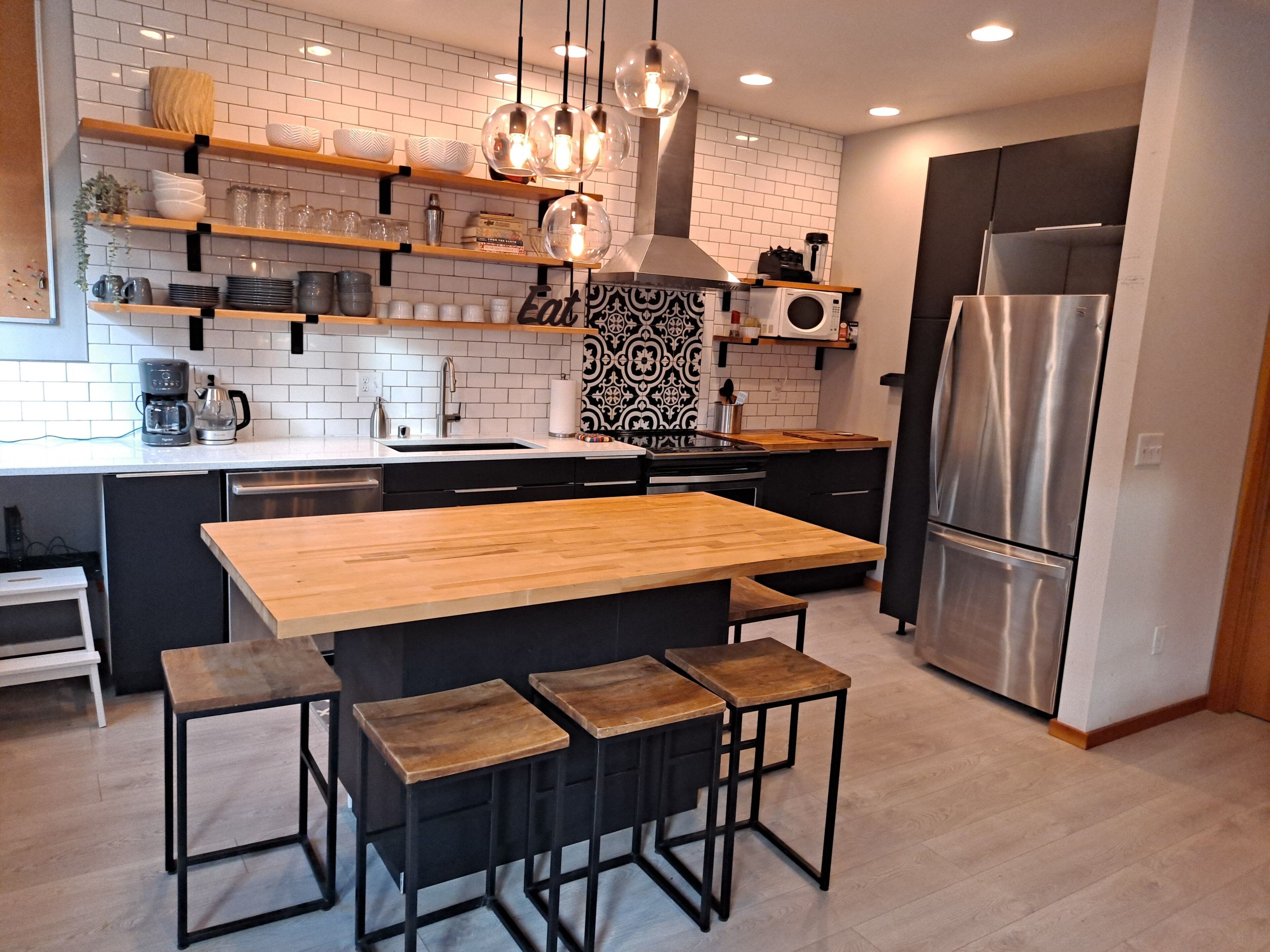 A modern kitchen with a central island, black cabinets, stainless steel appliances, and decorative shelves.