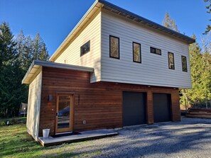 A modern two-story house with a combination of wooden and siding exterior, two garage doors, and a small porch area. - Northwest Modern 2-Bedroom on 5 private acres (Bellingham)