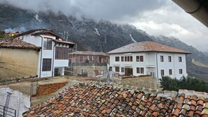 A mountainous village with traditional buildings, a visible waterfall, and a cloudy sky.
