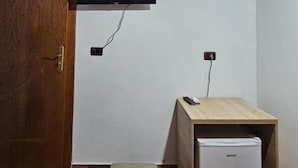 A room with a wooden door, a television mounted on the wall, and a small white refrigerator on a wooden cabinet.