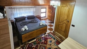 A room with a wooden ceiling, a bed with pillows, a patterned rug, and a door.