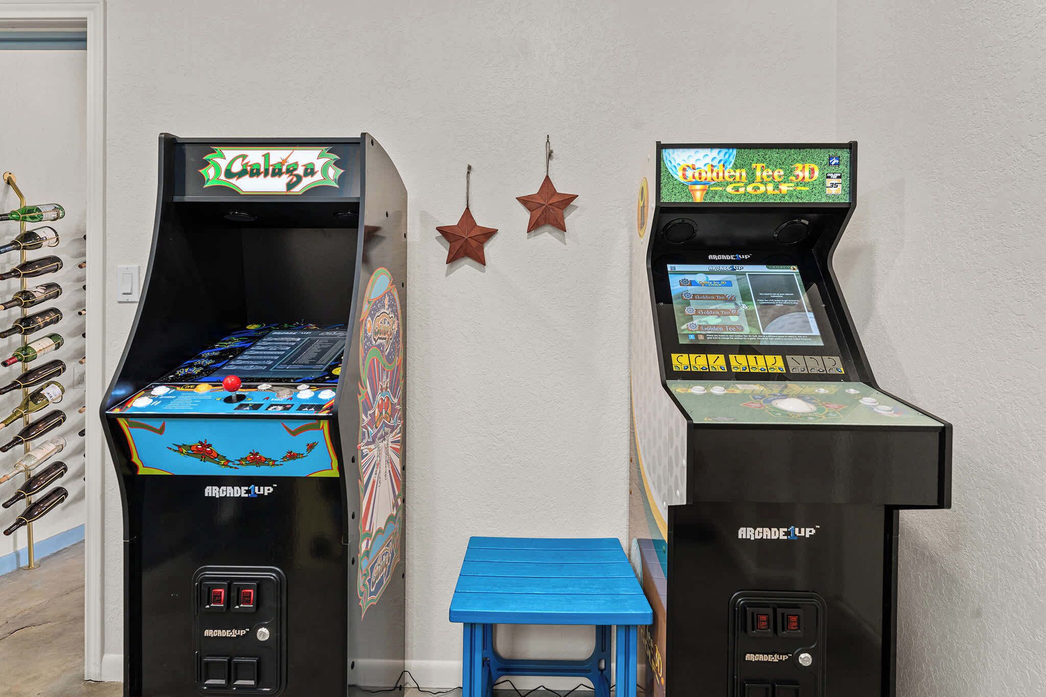 Two arcade machines, one labeled 'Galaga' and the other 'Golden Tee 3D Golf,' with a blue stool in front.