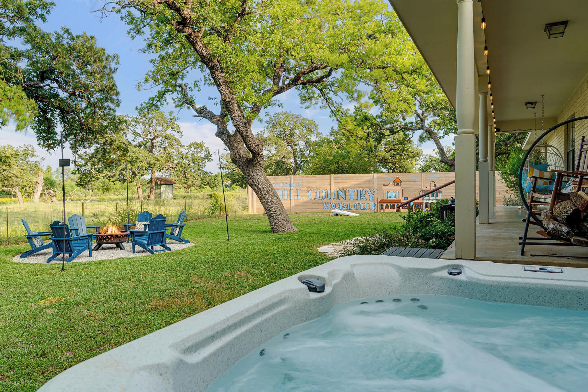 A hot tub with a fire pit, outdoor seating, and a covered area with a swing chair.