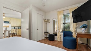 A hotel room with a bed, a blue armchair, a small table, a mirror, and a view of the kitchen. - 290 Wine Trail, 2 Hot tubs, Cowboy Pool, Game Room (Fredericksburg)