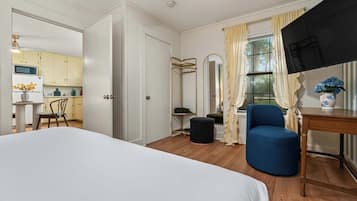 A hotel room with a bed, a blue armchair, a small table, a mirror, and a view of the kitchen.