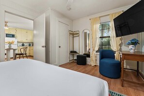 A hotel room with a bed, a blue armchair, a small table, a mirror, and a view of the kitchen. - 290 Wine Trail, 2 Hot tubs, Cowboy Pool, Game Room (Fredericksburg)