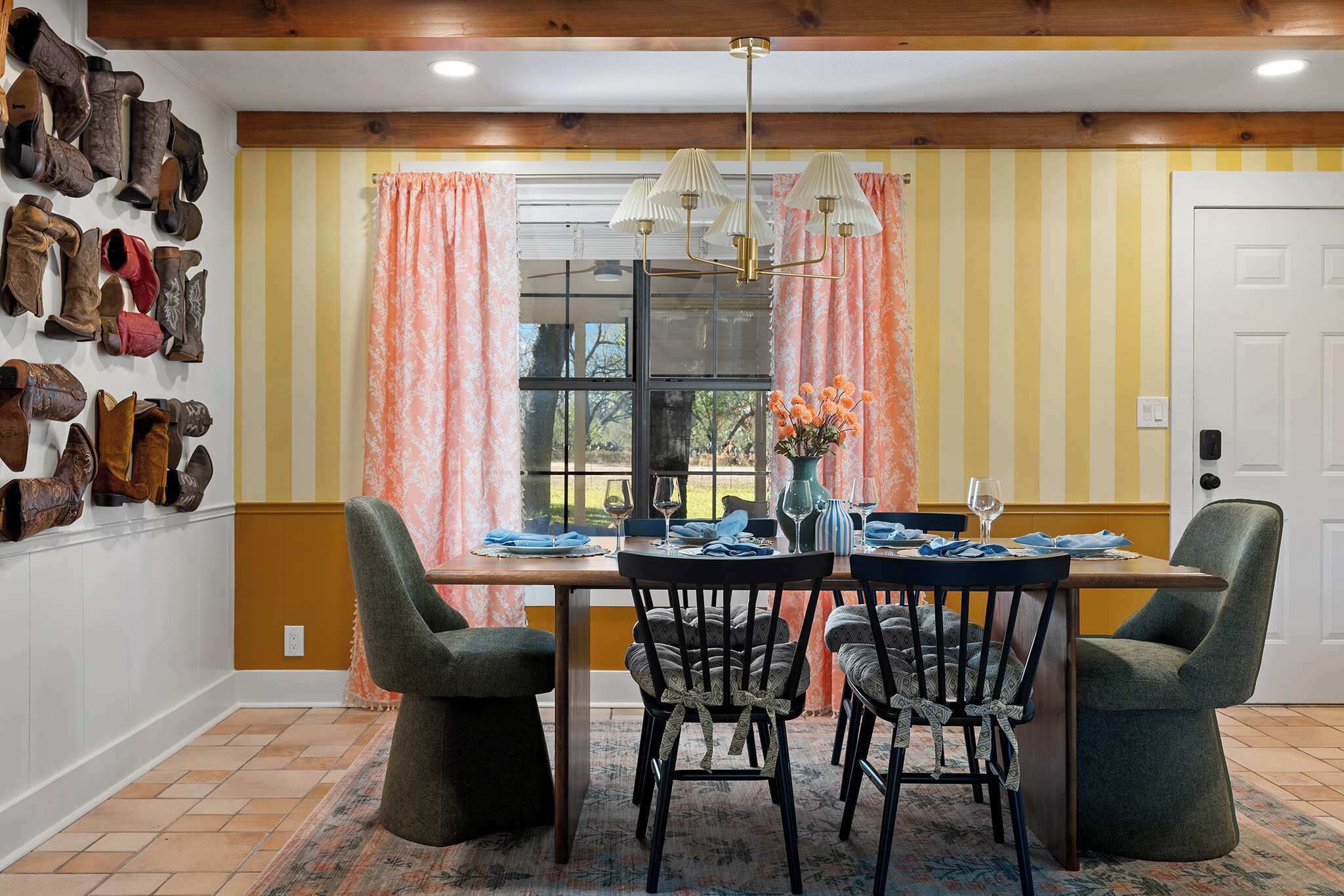A dining area with a wooden table, four chairs, a chandelier, and a window with curtains.