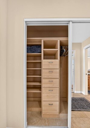 Ein begehbarer Kleiderschrank mit mehreren Regalen und Schubladen, einer Kleiderstange und einer Tür zu einem anderen Raum.