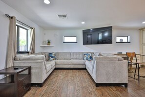 A modern living room with a sectional sofa, a wooden floor, and a flat-screen TV mounted on the wall. - Beautiful home on 2 full acres with a pool! (Citrus Park)