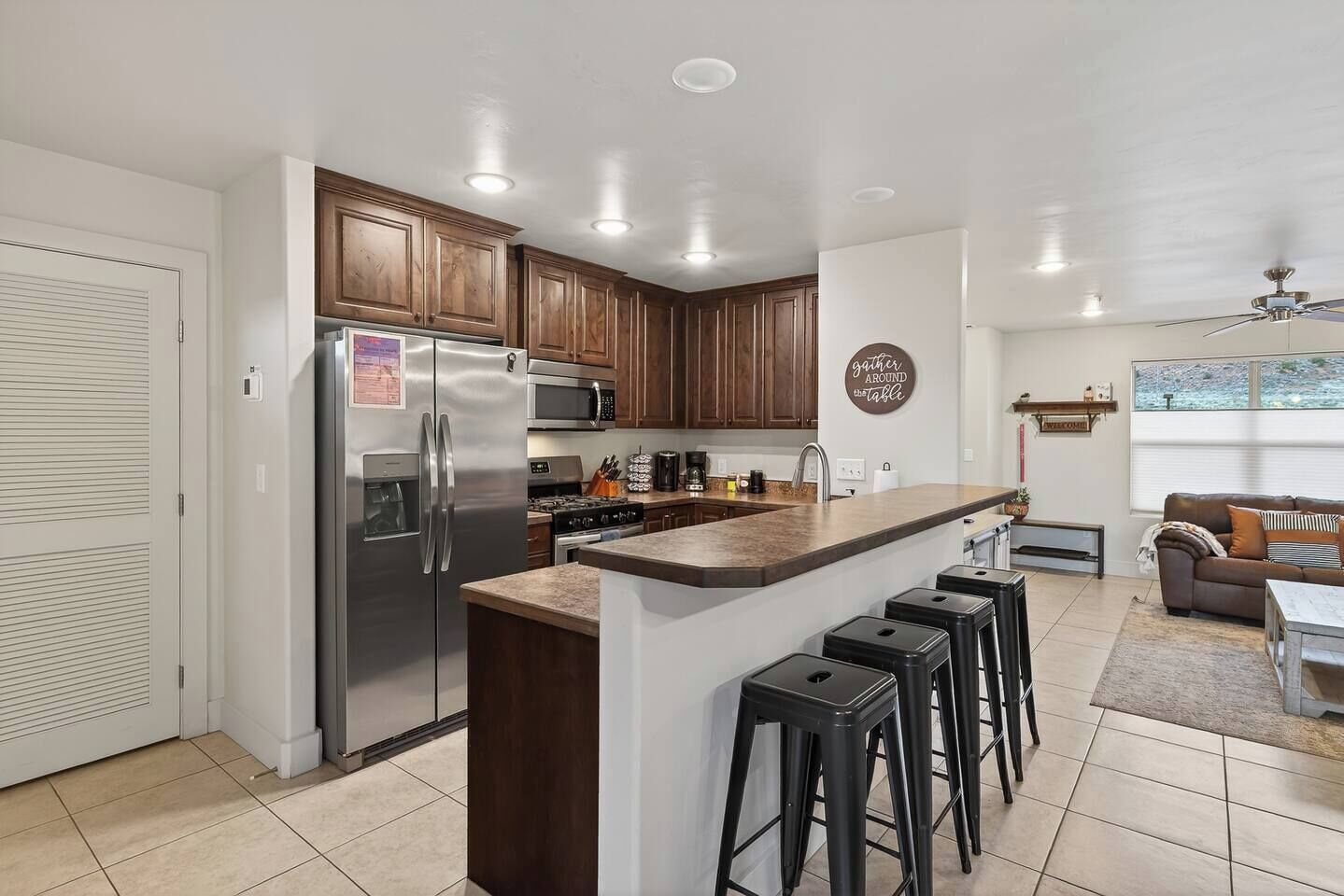 A modern kitchen with a central island, bar stools, wooden cabinets, and a built-in microwave.
