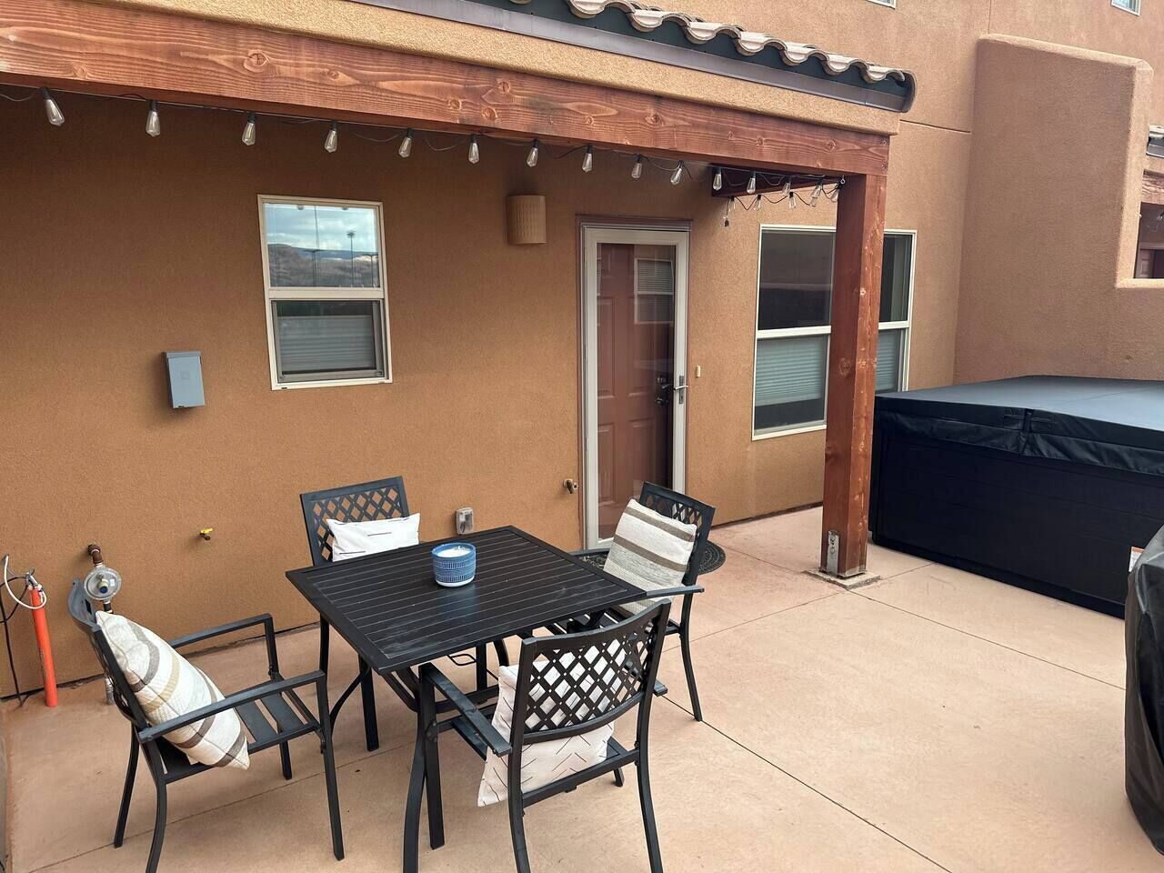 Un patio exterior con una mesa y sillas, un trampolín cubierto, y una puerta que da a la casa.