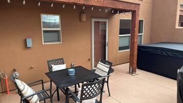 Un patio exterior con una mesa y sillas, un trampolín cubierto, y una puerta que da a la casa.