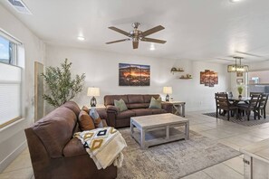 A living room with a brown leather sofa, a wooden coffee table, and a dining area with a wooden table and chairs.