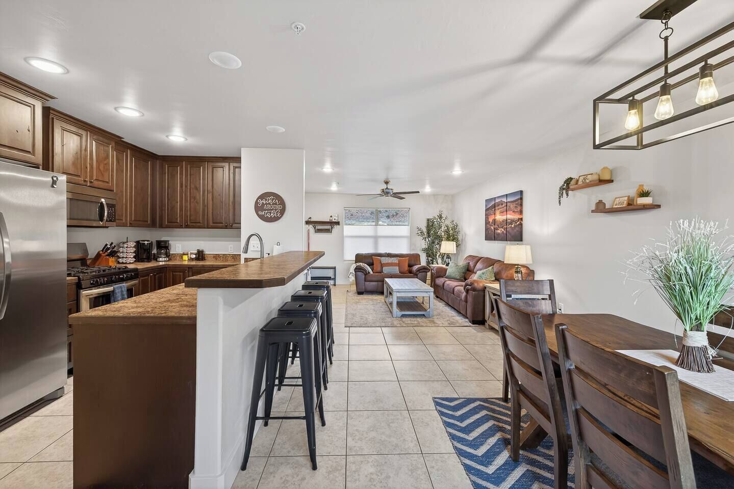 A modern kitchen with a central island, bar stools, and a dining area with a wooden table and chairs.