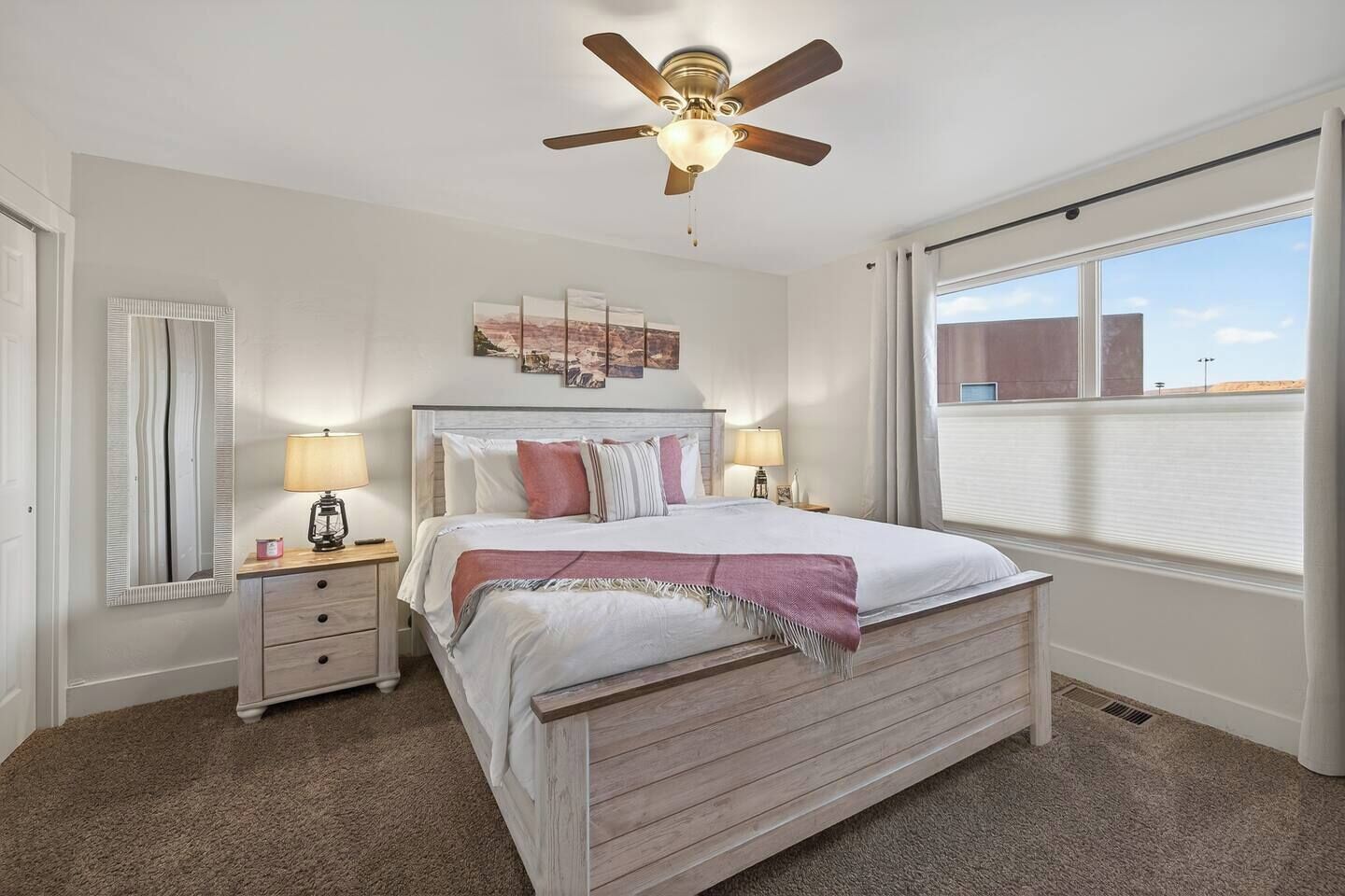 A bedroom with a bed, bedside lamps, a ceiling fan, a window with blinds, and a wall-mounted artwork.