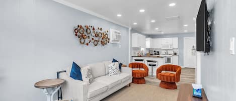A modern living room with a sofa, two armchairs, a coffee table, and a TV mounted on the wall.
