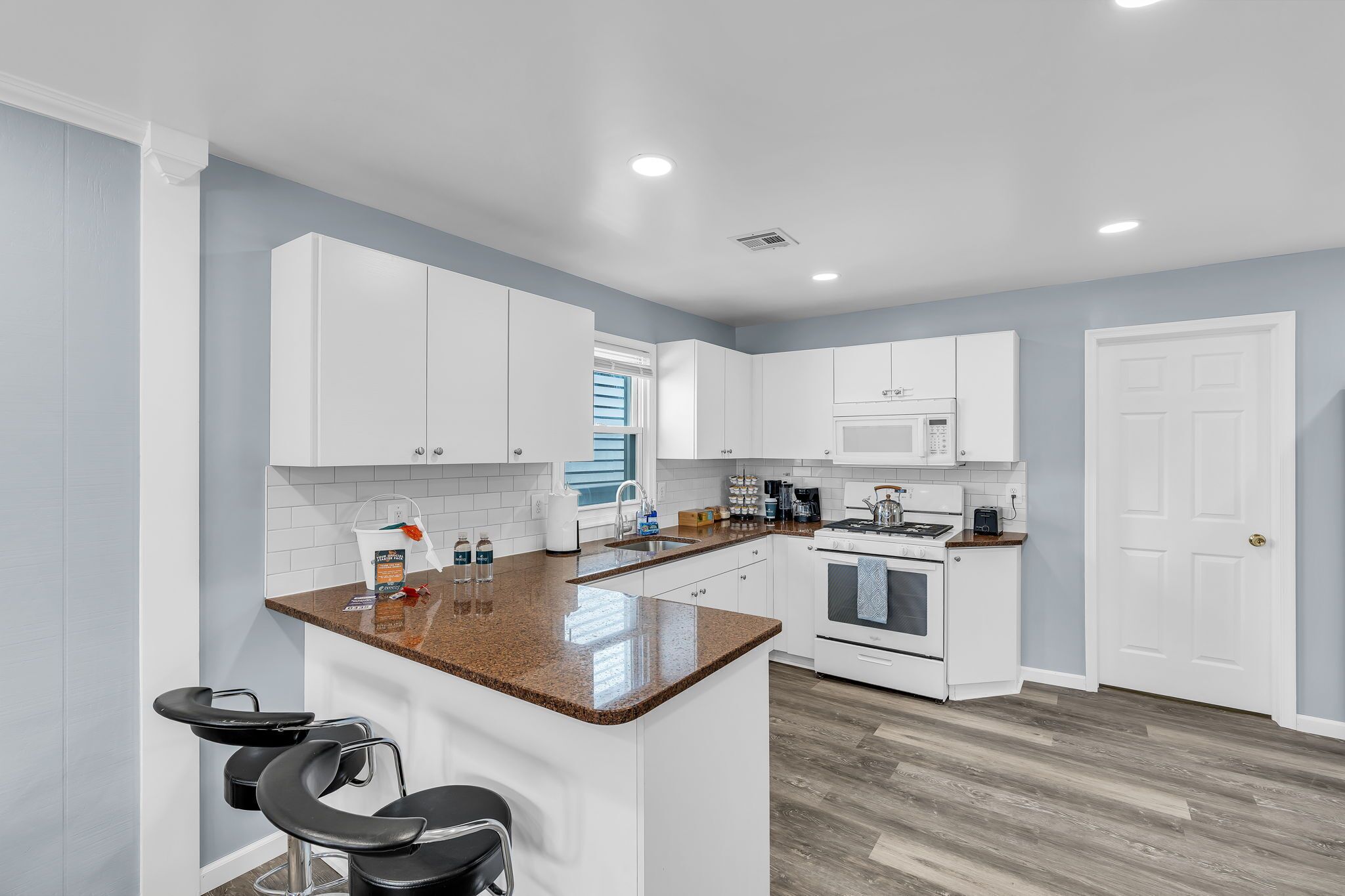 A modern kitchen with white cabinets, a granite countertop, a built-in oven, and a microwave.