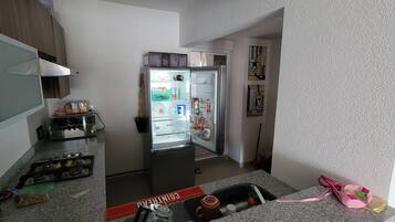 Een keuken met een koelkast, een magnetron en een spoelbak. Er staan verschillende spullen op het aanrecht, waaronder een fles, een beker en een zak.