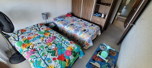 Un dormitorio con dos camas, un ventilador, una lámpara y una mesita.