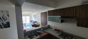 Una cocina moderna con estufa integrada, un lavamanos y una encimera. Se ve un rincón comedor al fondo con un sofá y una mesa.