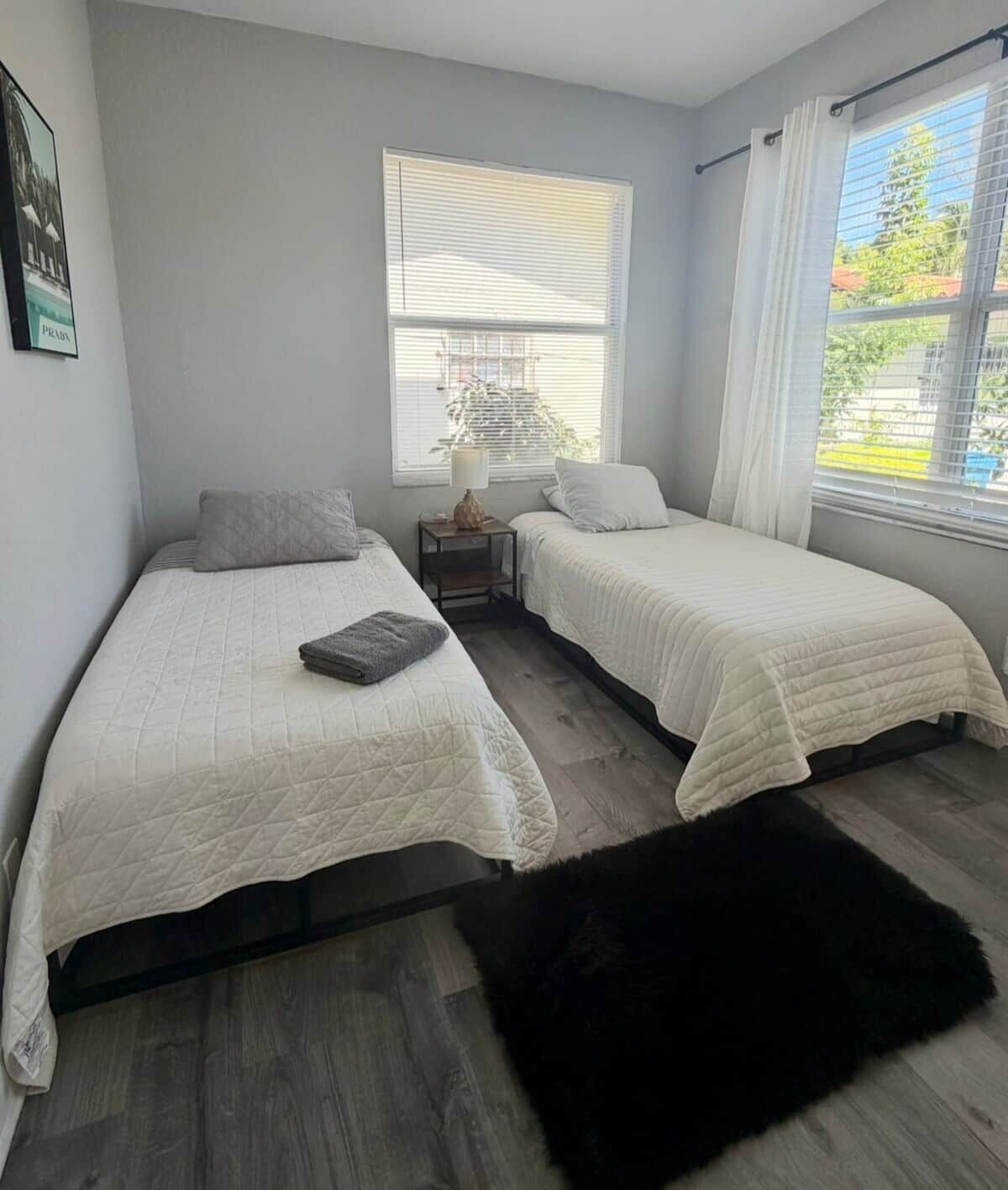 A bedroom with two beds, a nightstand, a lamp, and a window with curtains.