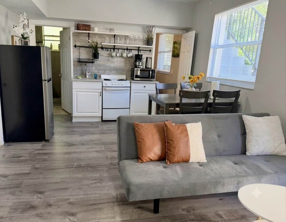 A modern kitchen with white cabinets, a black refrigerator, and a dining area with a gray sofa and chairs.