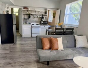 Eine moderne Küche mit weißen Schränken, einem schwarzen Kühlschrank und einem Essbereich mit grauem Sofa und Stühlen.