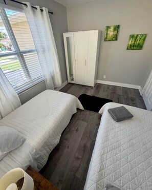 A bedroom with two beds, a wardrobe, and a window with curtains.