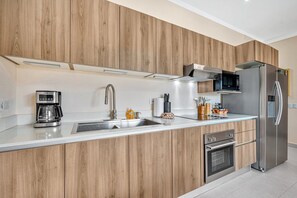 A modern kitchen with wooden cabinetry, a stainless steel refrigerator, a built-in oven, and a coffee maker. - Villa Ladera Laurel 10 | Luxe Hillside Retreat with Epic Views (Potrero)