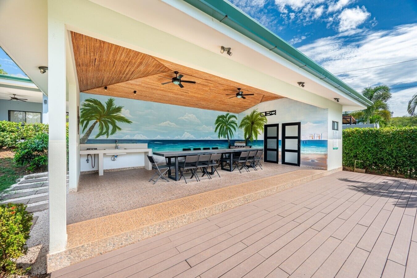 Una terrazza esterna con tavolo e sedie, una ventola a soffitto e un murale raffigurante una spiaggia.