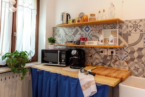 Una cocina con microondas, cafetera y juego de té en estantes.
