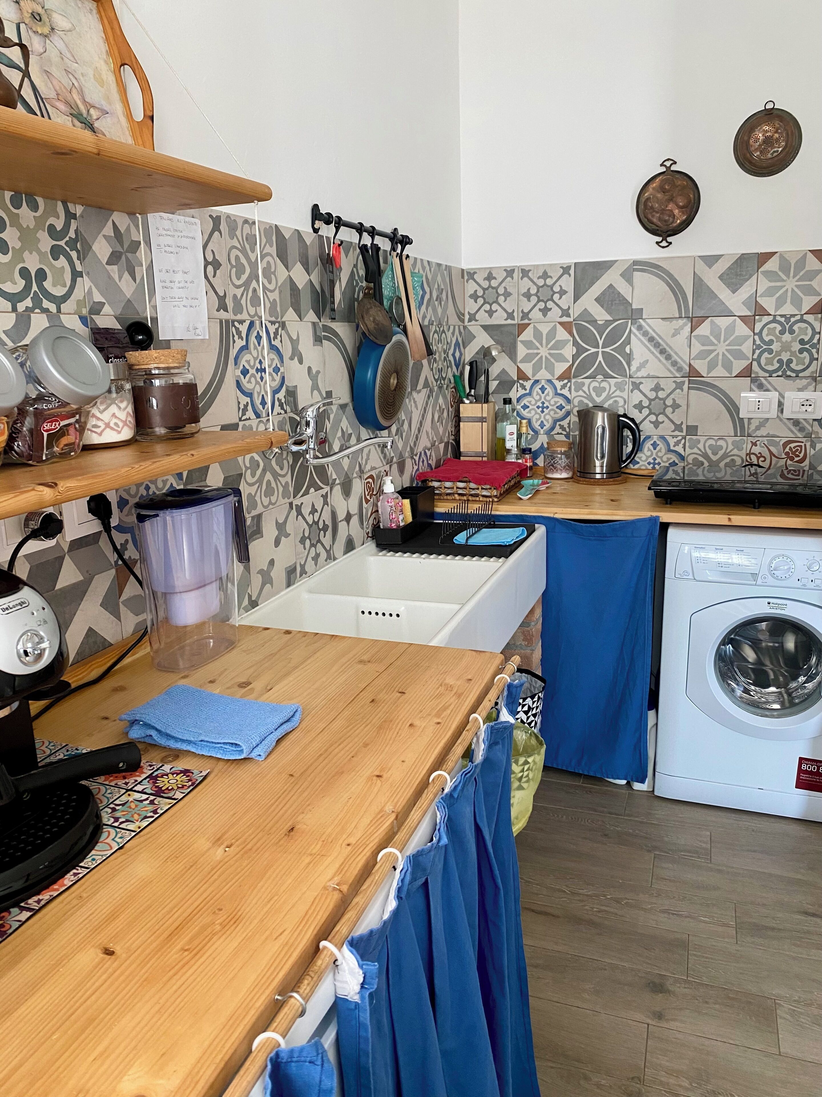 A kitchen with a wooden countertop, a washing machine, and a patterned backsplash.