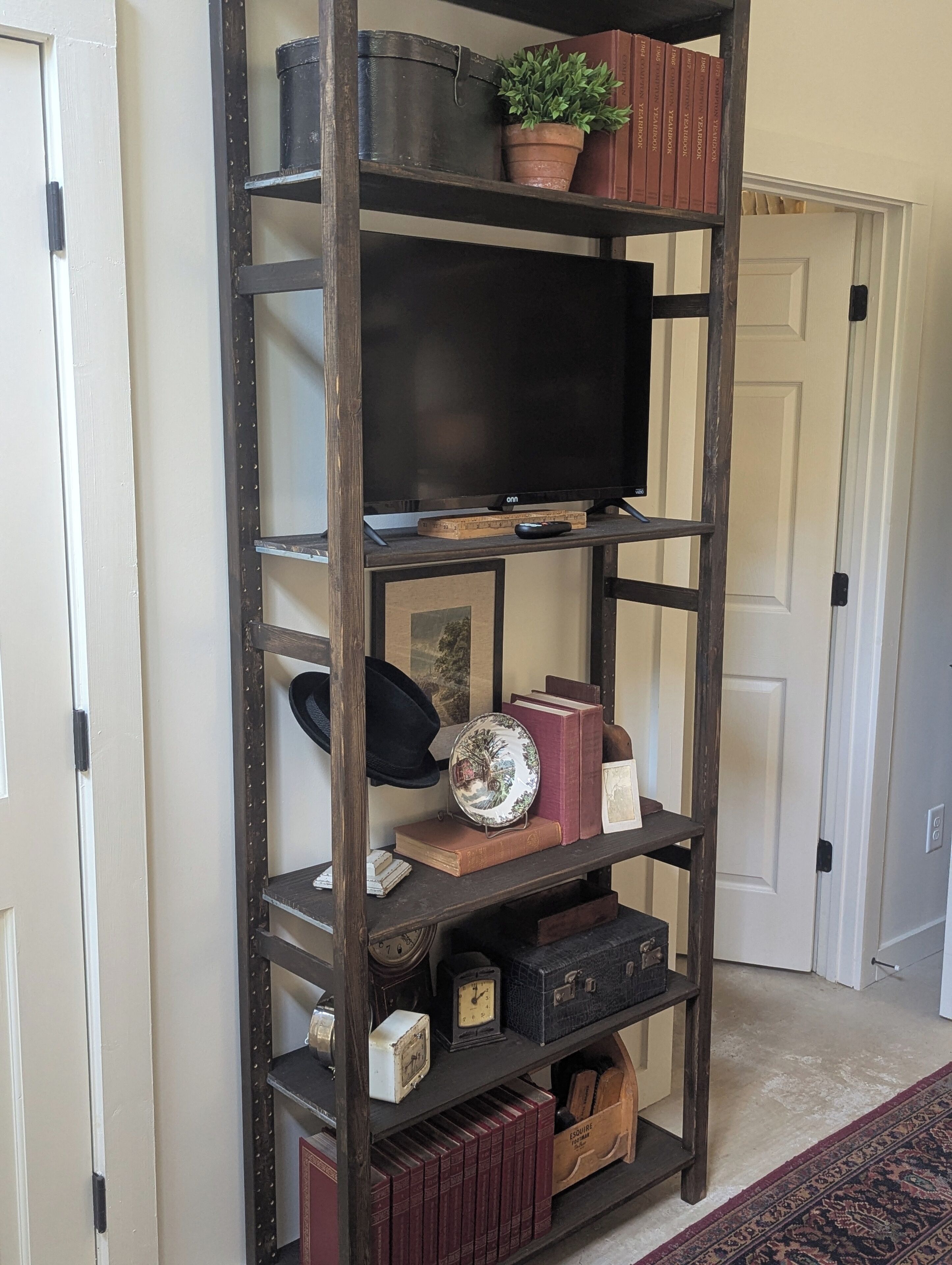 Una estantería de madera con un televisor, libros, objetos decorativos y cajas de almacenamiento.