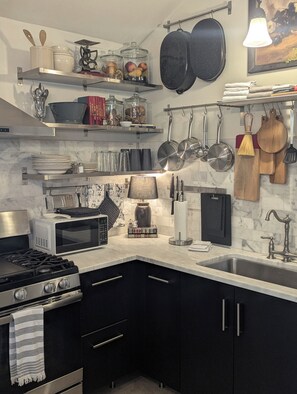 A modern kitchen with a gas stove, microwave, and a variety of utensils and cookware on the wall.