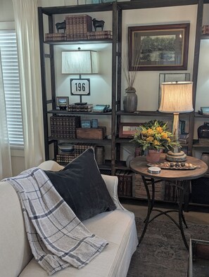 A cozy living room with a sofa, a coffee table, and a bookshelf filled with books and decorative items.