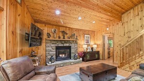 A wooden interior with a stone fireplace, leather furniture, and a staircase.