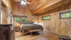Dormitorio de cabaña de madera con cama, banco y ventanas.
