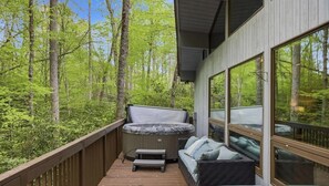 A hot tub on a wooden deck with a sofa and cushions, surrounded by a forest. - Home with Hot Tub, Conveniently located between Boone and Blowing Rock, (Boone)