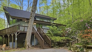 A two-story cabin with a wooden deck and a staircase leading to the upper level.